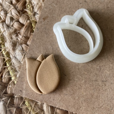 Cortador de biscoitos branco em forma de pétala com peças cortadas bege claro sobre cartão e fibras naturais