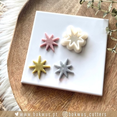 Três cortadores de massa estrelas coloridas sobre placa branca e base de madeira com folhas secas