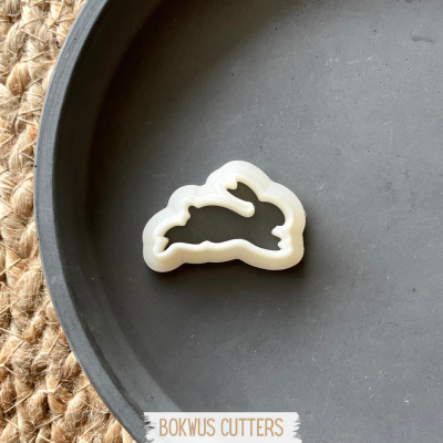 Cortador de massa em forma de coelho branco num prato preto sobre fundo de juta.