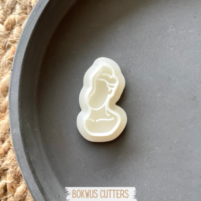 Corta-biscoitos branco em forma de figura feminina sobre prato preto