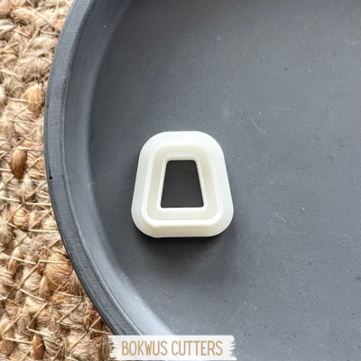 Cortador de massa branco em forma de trapézio sobre um prato preto e tapete de fibras naturais