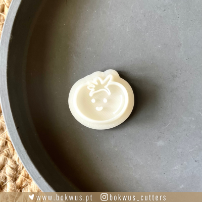 Cortador de bolachas de plástico branco em forma de tomate sorridente sobre prato cinzento