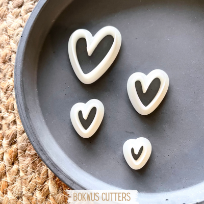 Quatro cortadores de biscoito em forma de coração branco num prato cinzento com superfície de palha.