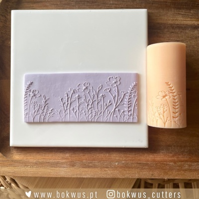 Carimbo retangular lilás com padrão floral e vela cilindrica bege com relevo floral sobre madeira