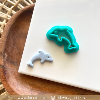 Cortador de bolacha golfinho verde água e mola de bolacha golfinho branco sobre superfície branca e bandeja de madeira.