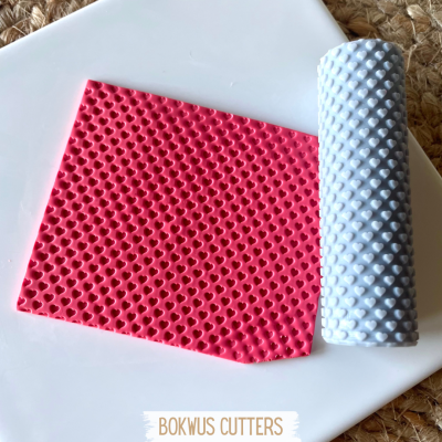 Tapete vermelho de silicone com padrão de corações e rolo cinzento com textura de bolhas sobre superfície branca