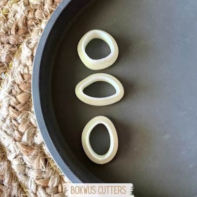 Três cortadores ovais brancos numa bandeja preta sobre juta trançada