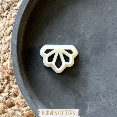 Cortador de bolachas branco geométrico sobre prato preto e fundo de rede natural.