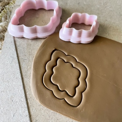 Moldes cor de rosa para cortar massa em formato floral sobre massa castanha numa superfície clara.