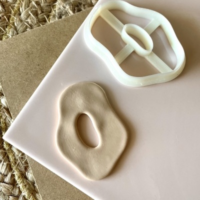 Cortador de massa branco e massa bege moldada em forma irregular com buraco oval