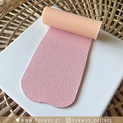 Rolo de massa rosa e laranja com textura pontilhada sobre prato branco em superfície trançada