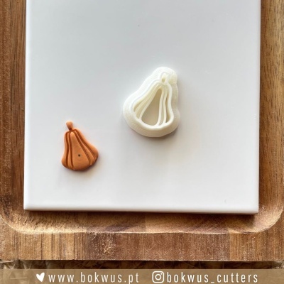 Dois cortadores de massa em forma de pêra, branco e laranja, sobre tabuleiro branco e base de madeira.