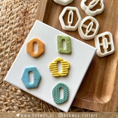 Cortadores de biscoitos geométricos em plástico branco e biscoitos em várias cores pastel com texturas em azulejo branco e tabuleiro de madeira.