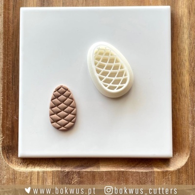 Cortador de silicone com padrão de abacaxi e selo de massa cor chocolate sobre superfície branca e tábua de madeira