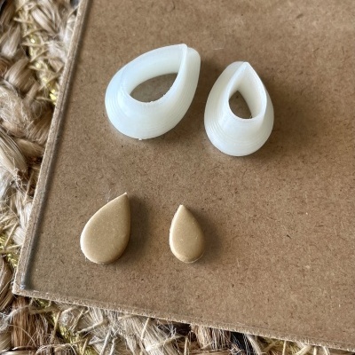 Quatro peças em forma de gota brancas e douradas sobre cartão e tapete de fibras naturais