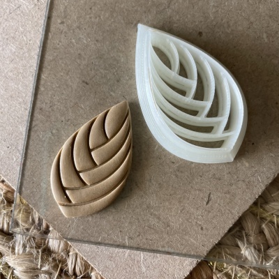 Moldes em forma de folha, branco e castanho, sobre madeira clara e tecido natural.