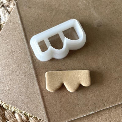 Cortante de três arcos branco e peça de massa dourada sobre cartão castanho