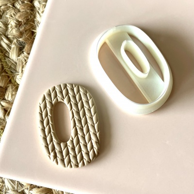 Dois cortadores ovais em creme e branco, um com padrão trançado e outro liso, sobre superfície clara.