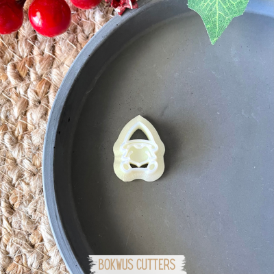 Cortante de massa creme formato Natal em prato cinza com decorações vermelhas e fundo de tecido trançado