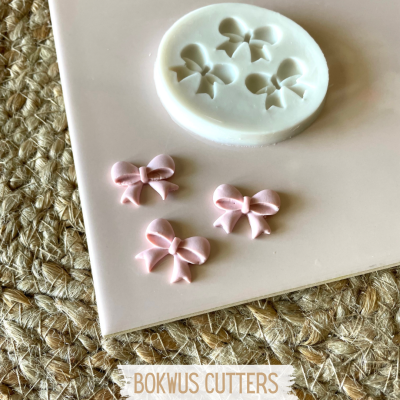 Molde de silicone branco para laços com três laços rosa em cima de superfície rosa clara e tapete de juta