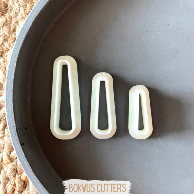 Três cortadores trapezoidais brancos dentro de uma tigela cinza sobre fundo de fibra natural.