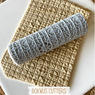Rolo de cortadores BOKWUS para massas cinza com padrão detalhado sobre massa dourada texturizada