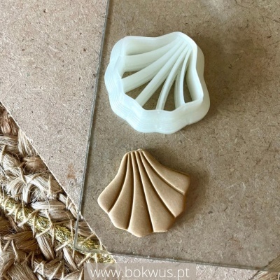 Dois moldes em forma de concha, um branco e outro castanho claro, sobre superfícies de pedra e tapete de fibras.