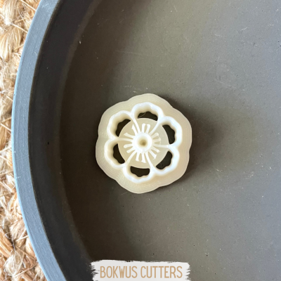 Cortador de massa em forma de flor bege claro dentro de recipiente cinza.