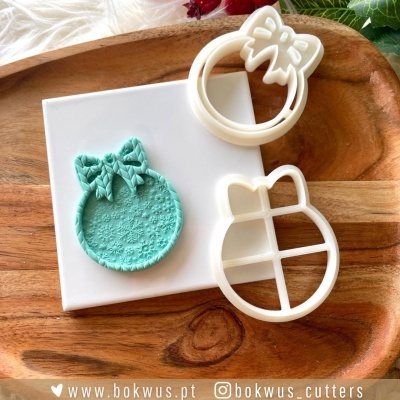 Cortadores de bolachas de plástico branco e pasta modelável verde menta em forma de bola de Natal com laço sobre tábua de madeira