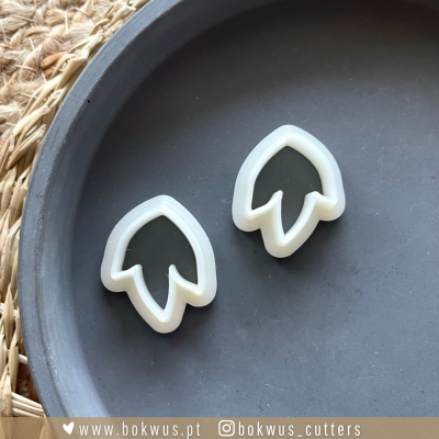 Dois cortadores de massa brancos em forma de pétala de flor sobre prato preto redondo