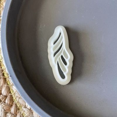 Cortador de bolachas em forma de pena dentro de um prato cinzento sobre base de fibra natural.