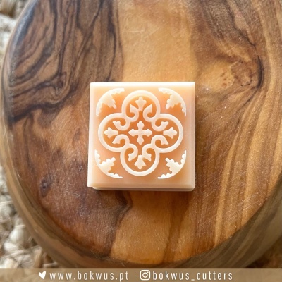 Cortador de biscoitos quadrado laranja com padrão decorativo branco sobre tábua de madeira