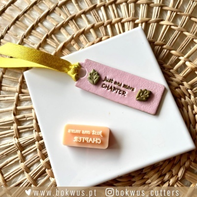 Marcador rosa em pele com texto e cordão amarelo sobre prato branco e base trançada de palha