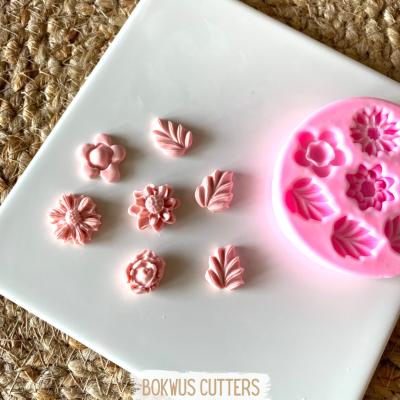 Molde de silicone rosa com formas de flores e folhas e peças moldadas na mesma cor sobre prato branco