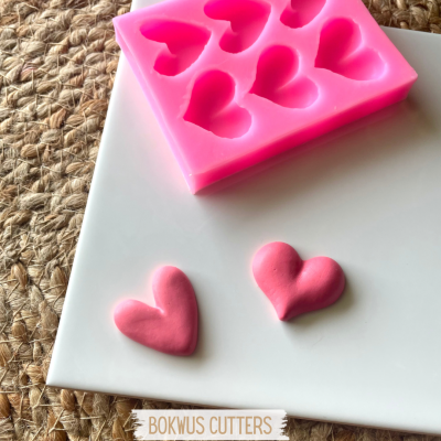 Moldes de silicone rosa em formato de corações com corações rosa feitos, sobre base branca e superfície de fibra natural