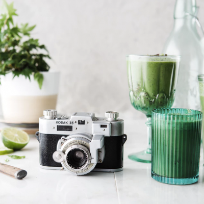 Câmara Kodak 35 antiga com copos verdes e planta sobre mesa branca