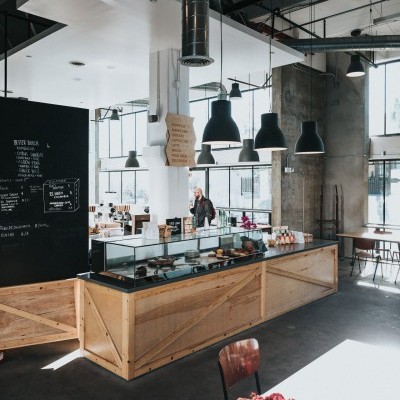 Cafetaria com balcão de madeira, iluminação pendente e flores cor-de-rosa em mesa.