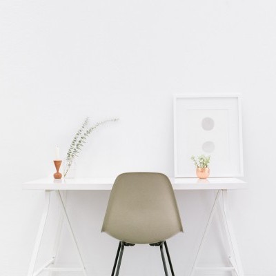 Secretária branca com cadeira cinzenta e objetos decorativos minimalistas.