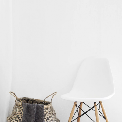 Cesto trançado com pano cinzento ao lado de cadeira branca com pernas de madeira