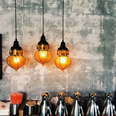Três lâmpadas pendentes laranja com bancada de madeira, garrafas metálicas com texto chinês e parede cinza