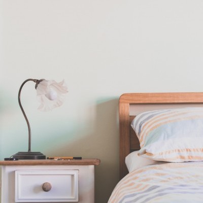 Cama com roupa de cama às riscas e mesa de cabeceira branca com candeeiro de flor.