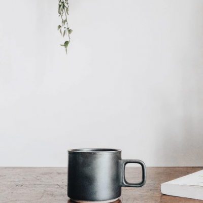 Caneca preta de cerâmica em mesa de madeira com planta pendente ao fundo