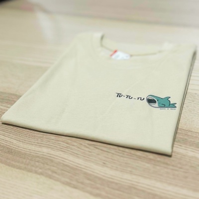 Camisola bege clara dobrada com estampa de tubarão e texto no peito