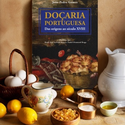 Livro sobre doçaria portuguesa com ingredientes de pastelaria ao redor numa mesa de madeira