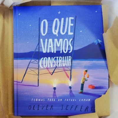 Capa de livro azul e roxo com título O QUE VAMOS CONSTRUIR e ilustração de homem e criança
