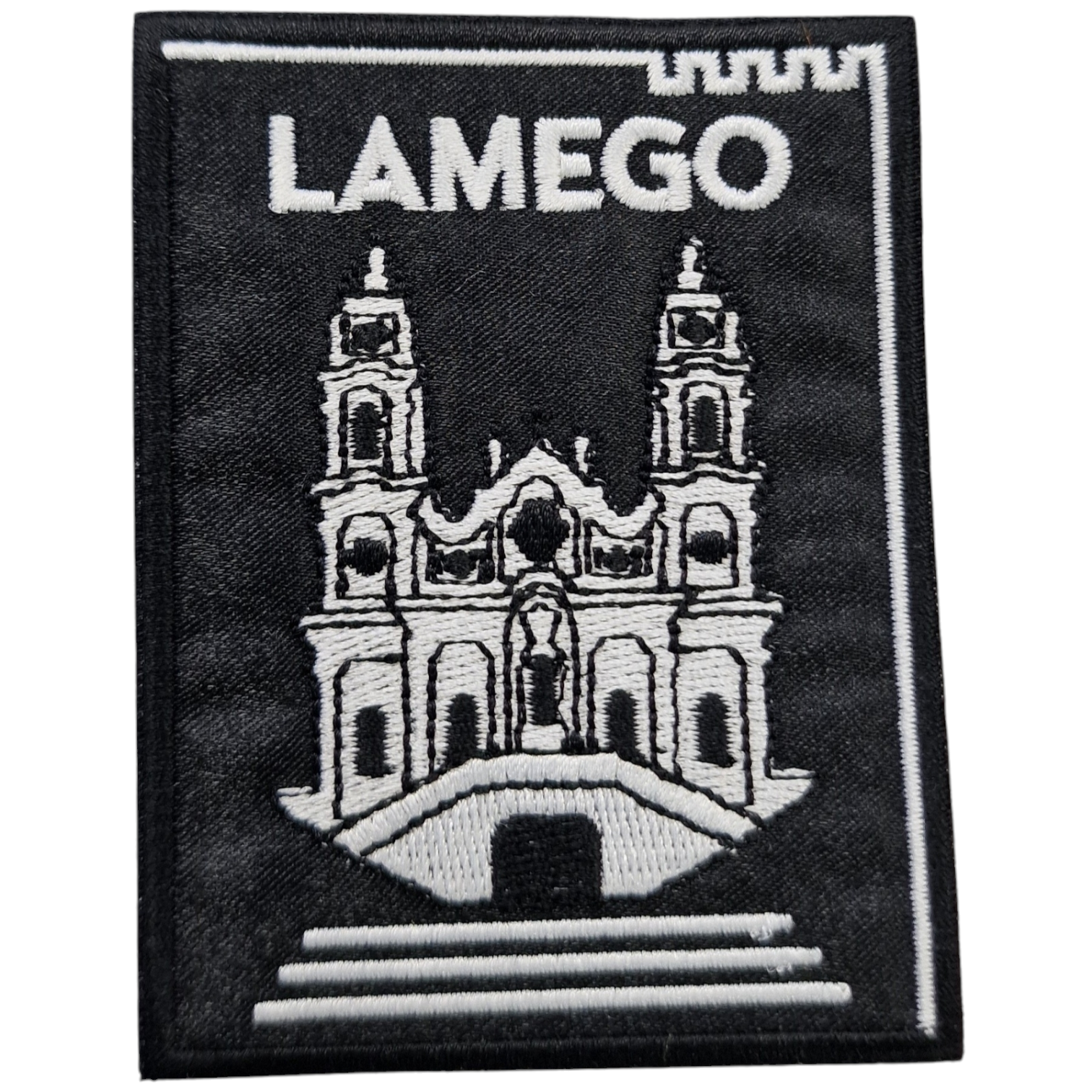 Pano bordado preto com desenho branco de edifício e texto LAMEGO