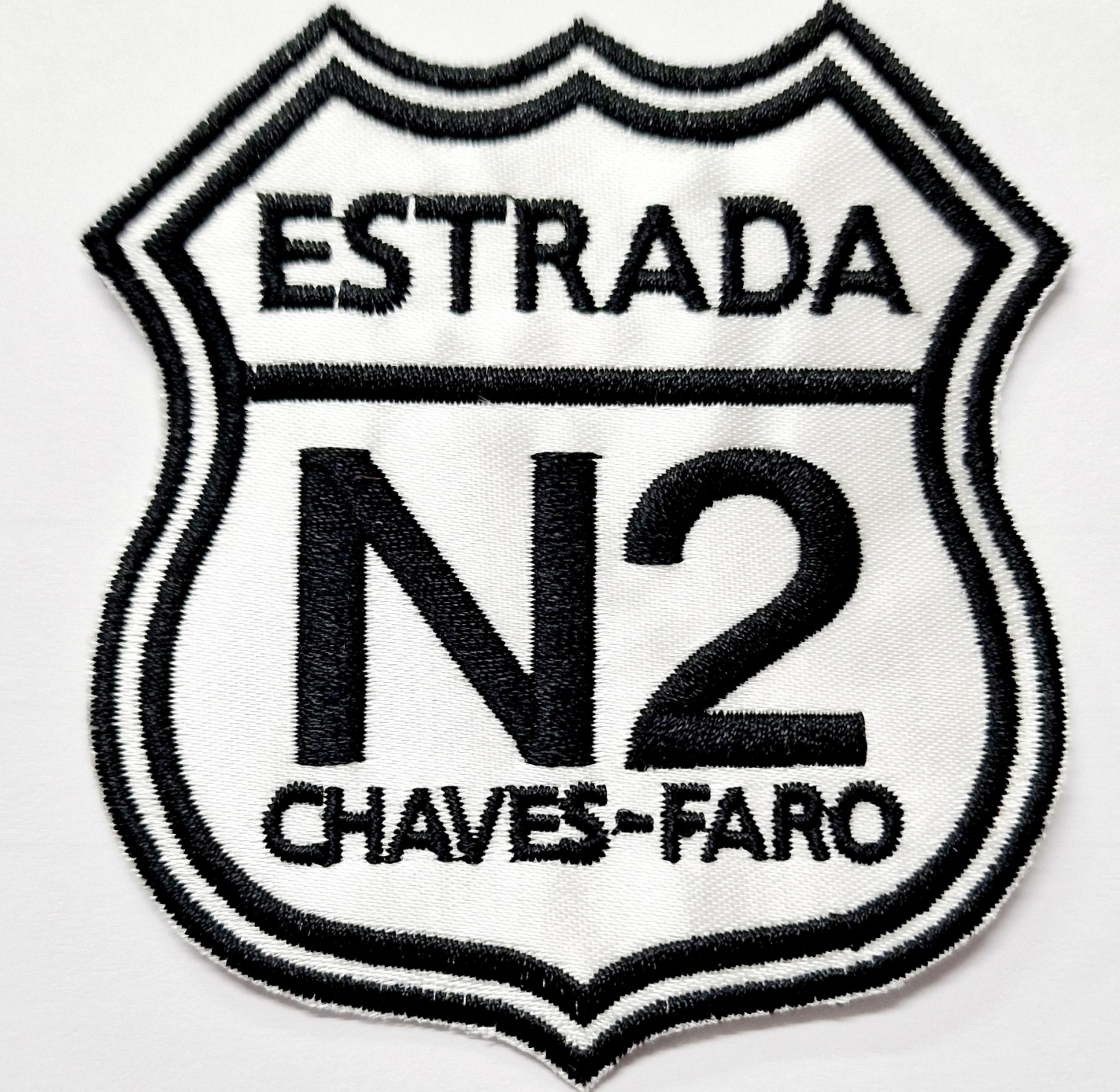 Emblema bordado preto e branco com texto ESTRADA N2 CHAVES-FARO