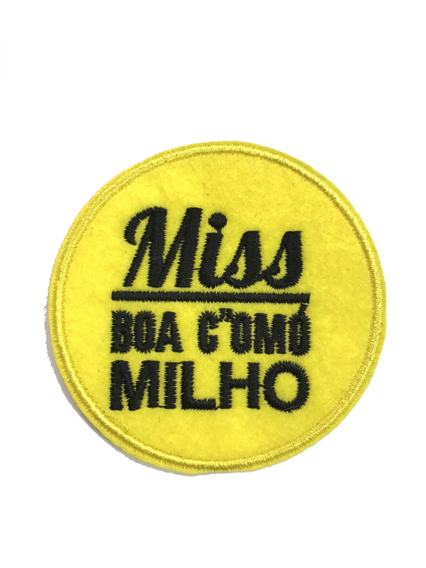 Emblema redondo amarelo com texto bordado preto 'Miss BOA COMÚ MILHO'