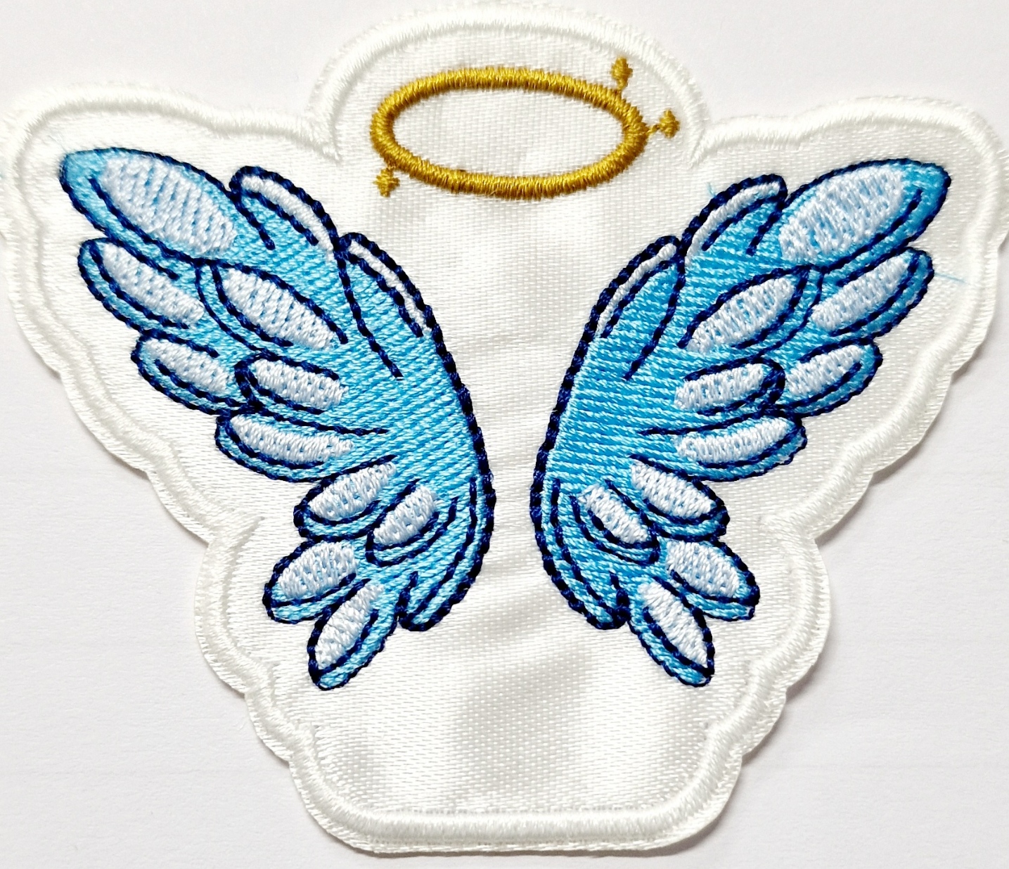 Aplicação bordada asas de anjo azuis com auréola amarela em tecido branco