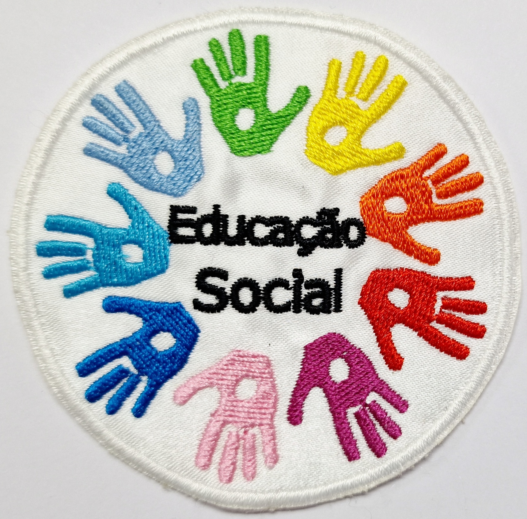 Emblema bordado circular com mãos coloridas e texto Educação Social